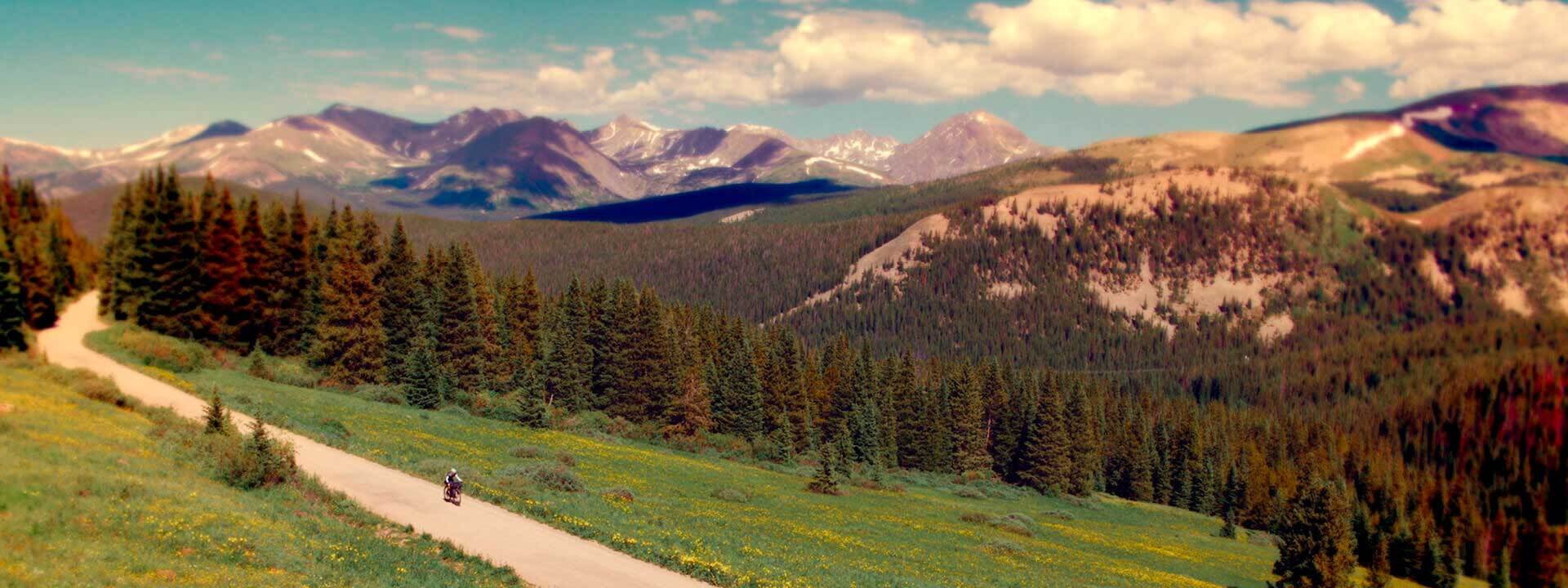 Cyclist riding on mountain gravel road at high elevation, mountain range in background