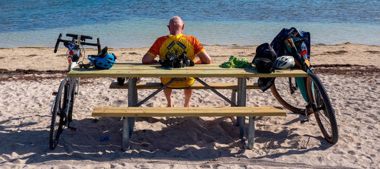 Gunner enjoying the sandy beach sitting at picnic table bikes parked shoes off