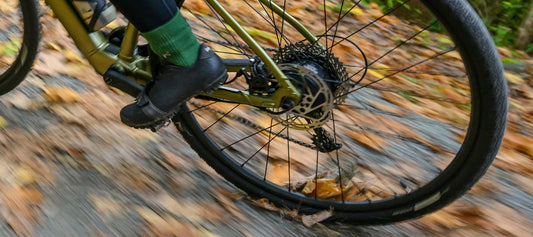 Close-up of cyclist skidding rear wheel of Salsa Confluence Drop Bar Ebike on gravel road with fall leaves