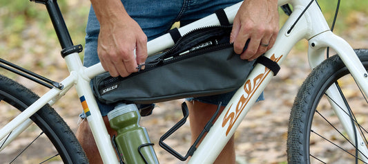 Cyclist standing with bike showing Salsa EXP Series Cholla Half-Frame Pack opening zipper on Salsa Journeyer