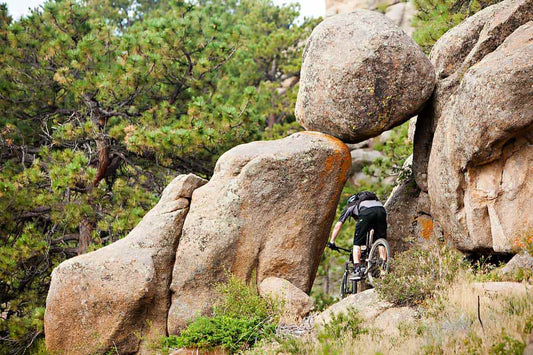 Mountain biker on trail riding through rocky tunnel with huge boulder overhead supported by massive rocks on either side