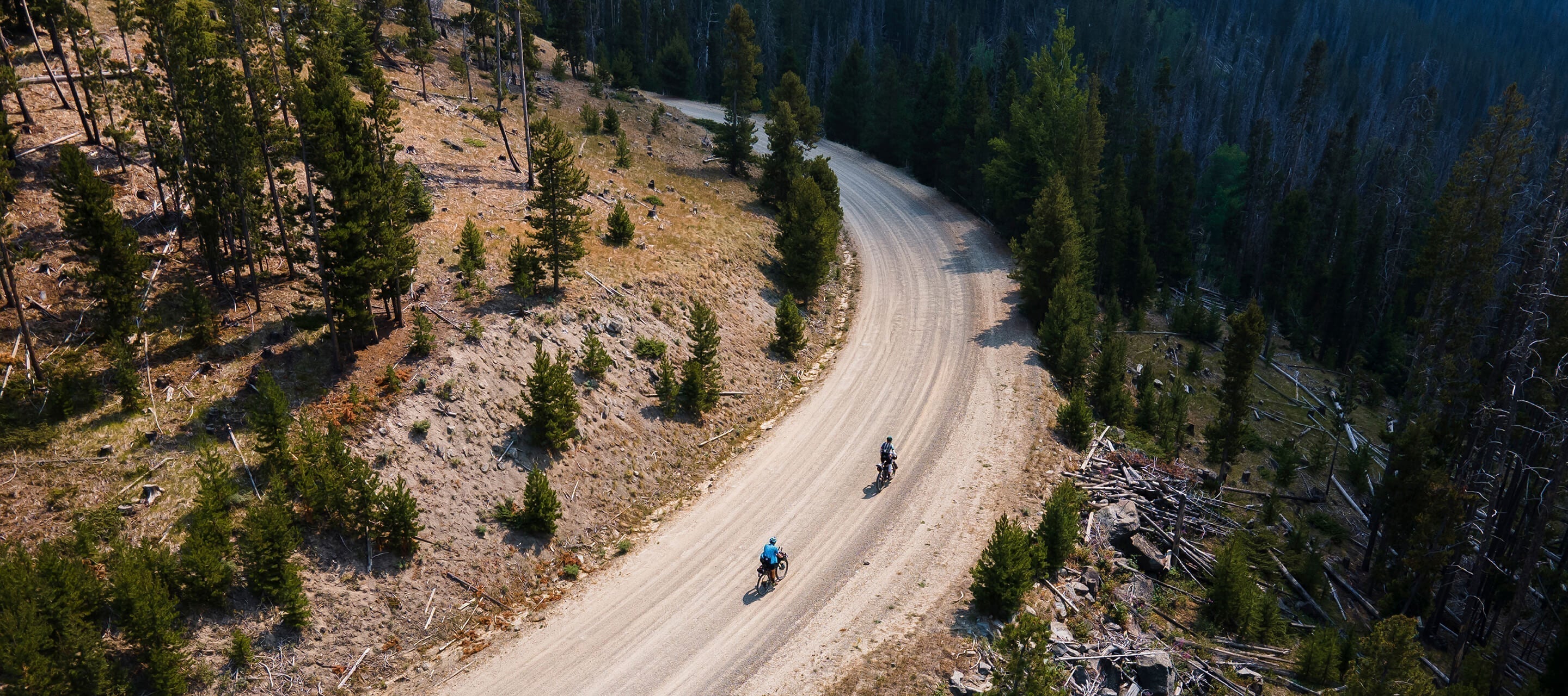 Drone shot of two cyclists riding around a curve on a  gravel road.