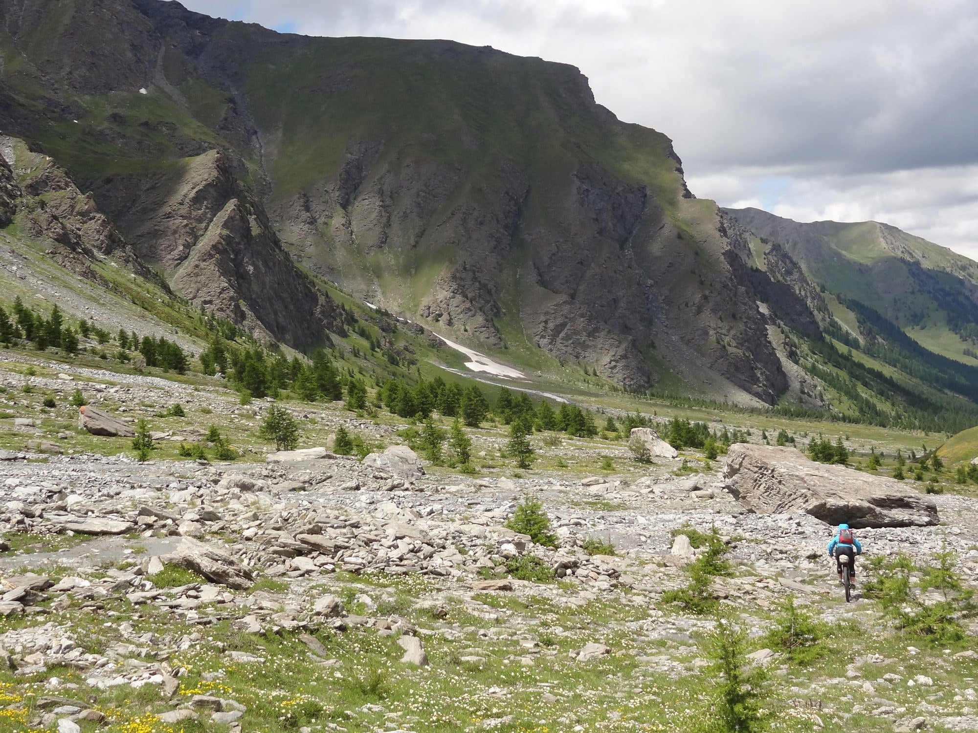 Kaitlyn descending a rocky alpine trail on loaded mountain bike with rocky peaks in background