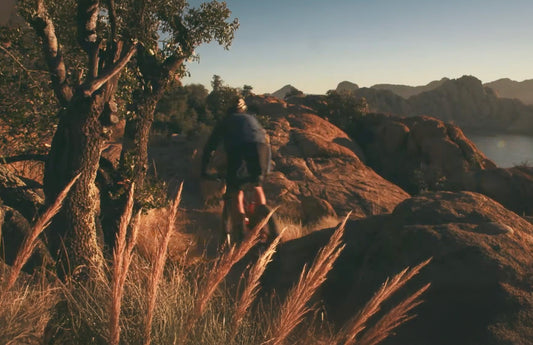 Cyclist shown from behind rides on a rocky cliffside trail during sunset