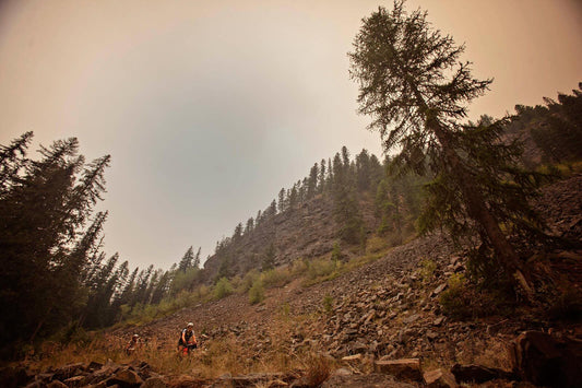 Laura and Trina riding loaded Salsa Cutthroat bikes on rock mountain road, photo taken lower down on rock fall, looking up