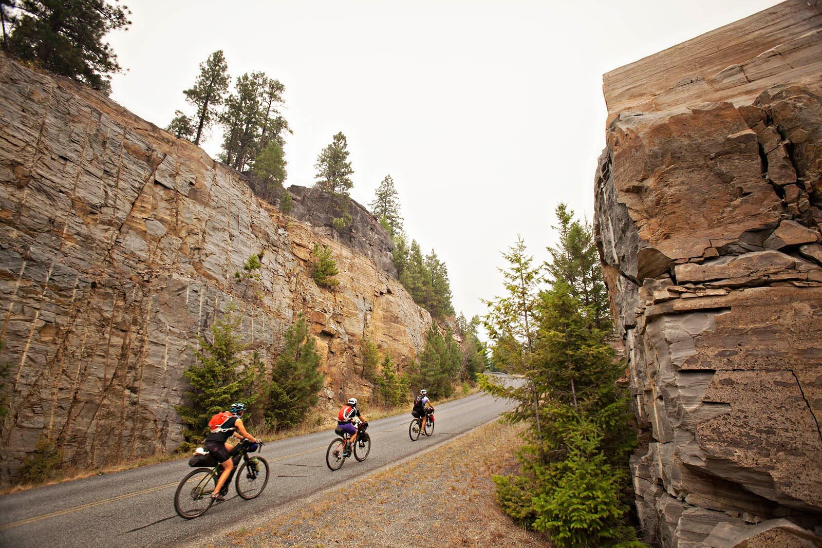 Laura, Trina, and Kelly climb paved mountain on loaded bikes, cliffs on both sides of road, air filled with smoke