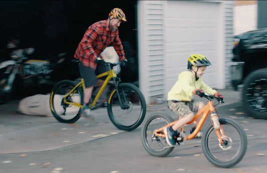 A parent and child ride their bikes together in the driveway.