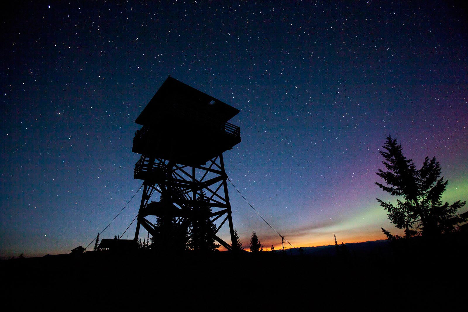 Fire tower at sunset, stars out on clear night, green arura borealis near horizon