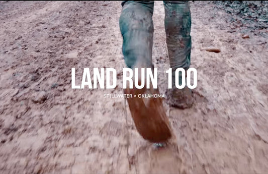 Closeup view of feet running along a muddy path. The title "Land Run 100" is in the center.