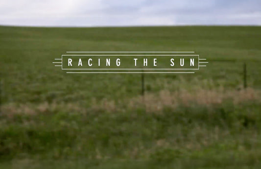 A rolling green meadow landscape with blue skies above. The title "Racing the Sun" is in the center.