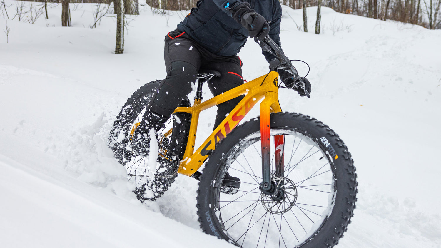 Cyclist rides an orange Salsa Beargrease fatbike through deep snow.