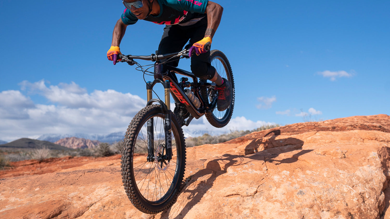 Mountain biker gets air over red rocks while riding a Salsa Blackthorn full suspension bike.