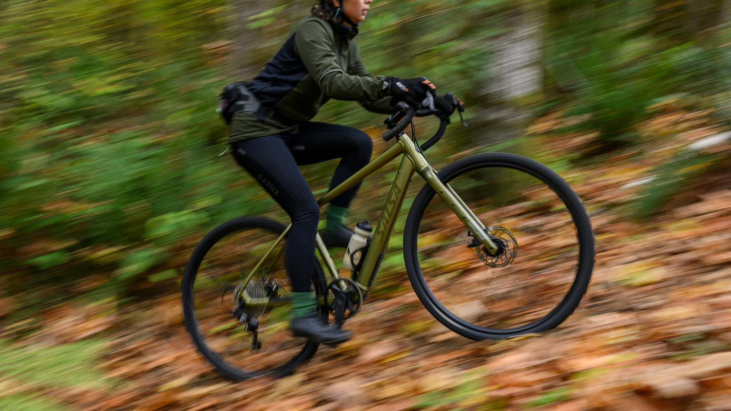 Cyclist rides a green drop bar Salsa Confluence ebike. They are riding uphill fast over leaves.