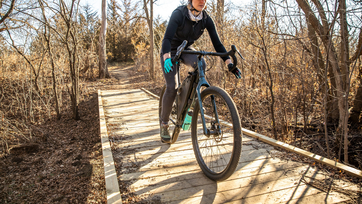 Cyclist rides a Salsa Fargo drop bar bike over a wooden bridge.