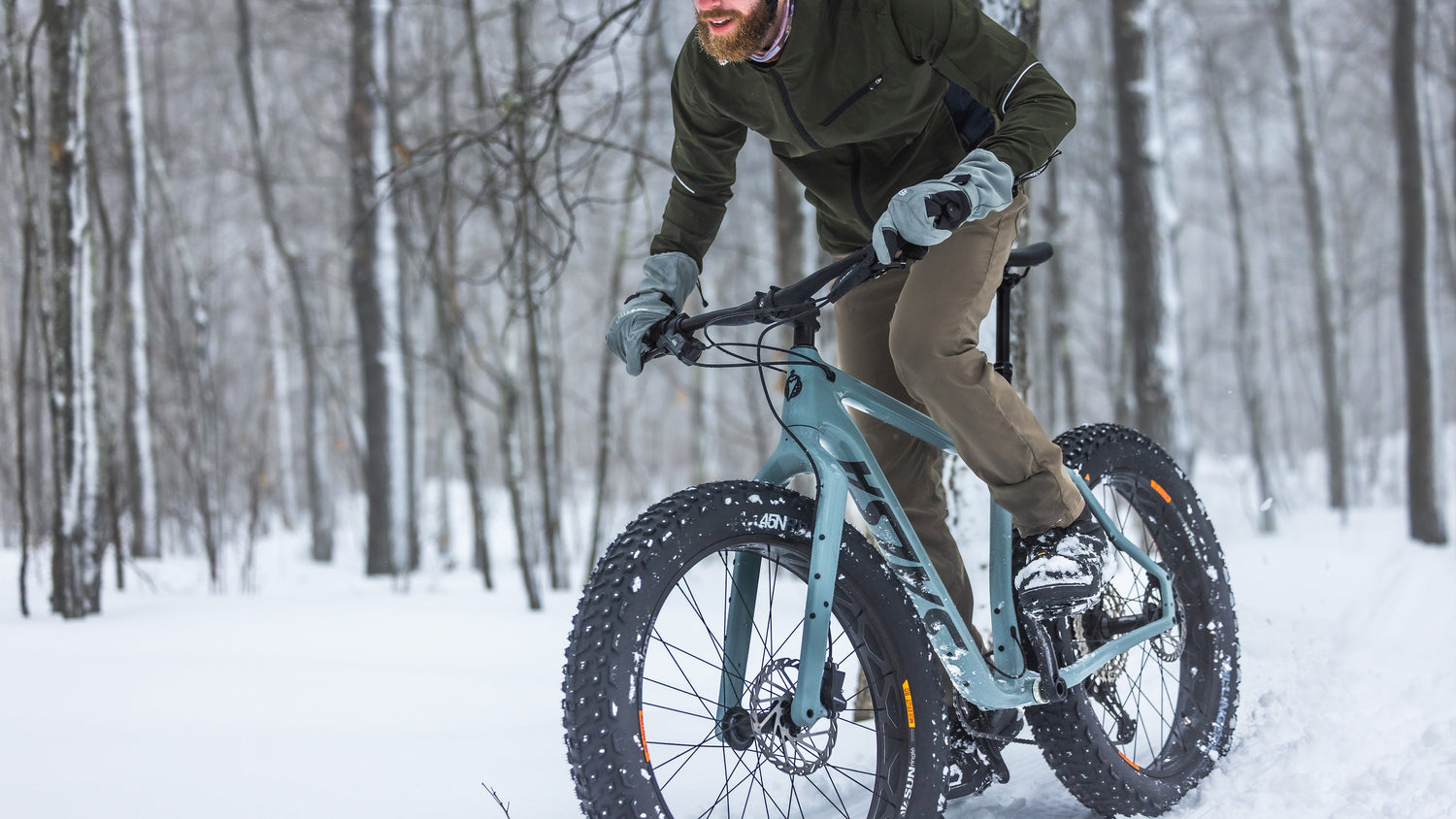 Cyclist rides a blue Salsa Heyday fatbike through snow. 