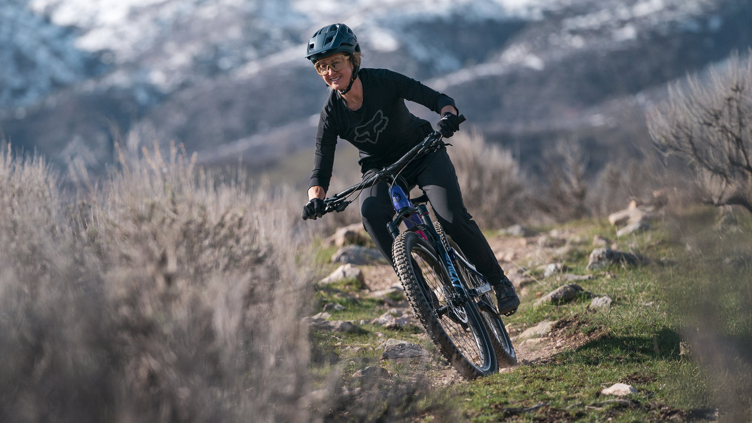 Mountain biker rides a Salsa Rustler full suspension bike on a trail.