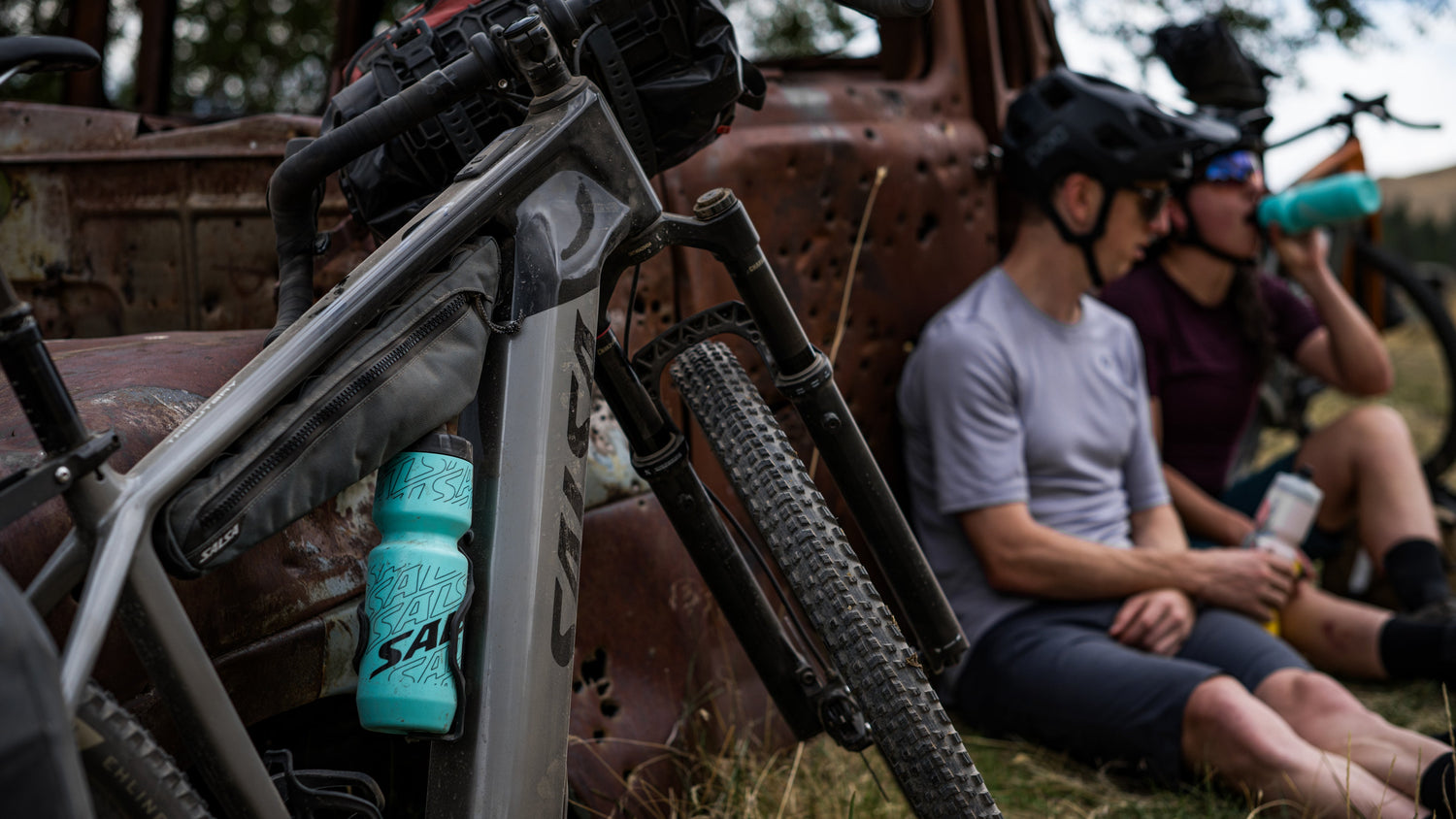 Cyclists take a water break next to a dark gray Salsa Tributary ebike.