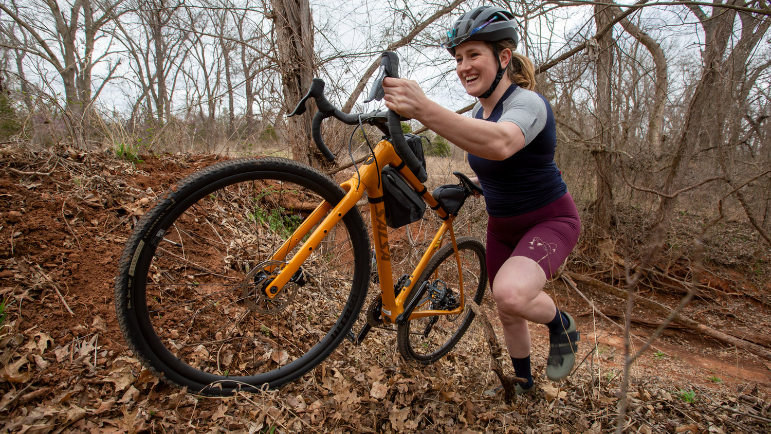 Cyclist hikes their orange Salsa Warbird drop bar bike uphill.