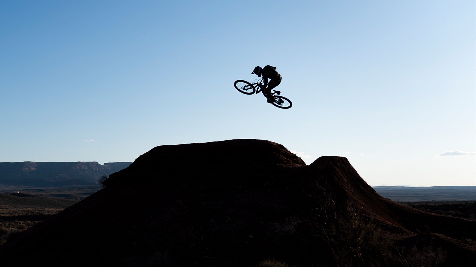 Mountain biker makes a huge jump on a dirt trail at dusk.