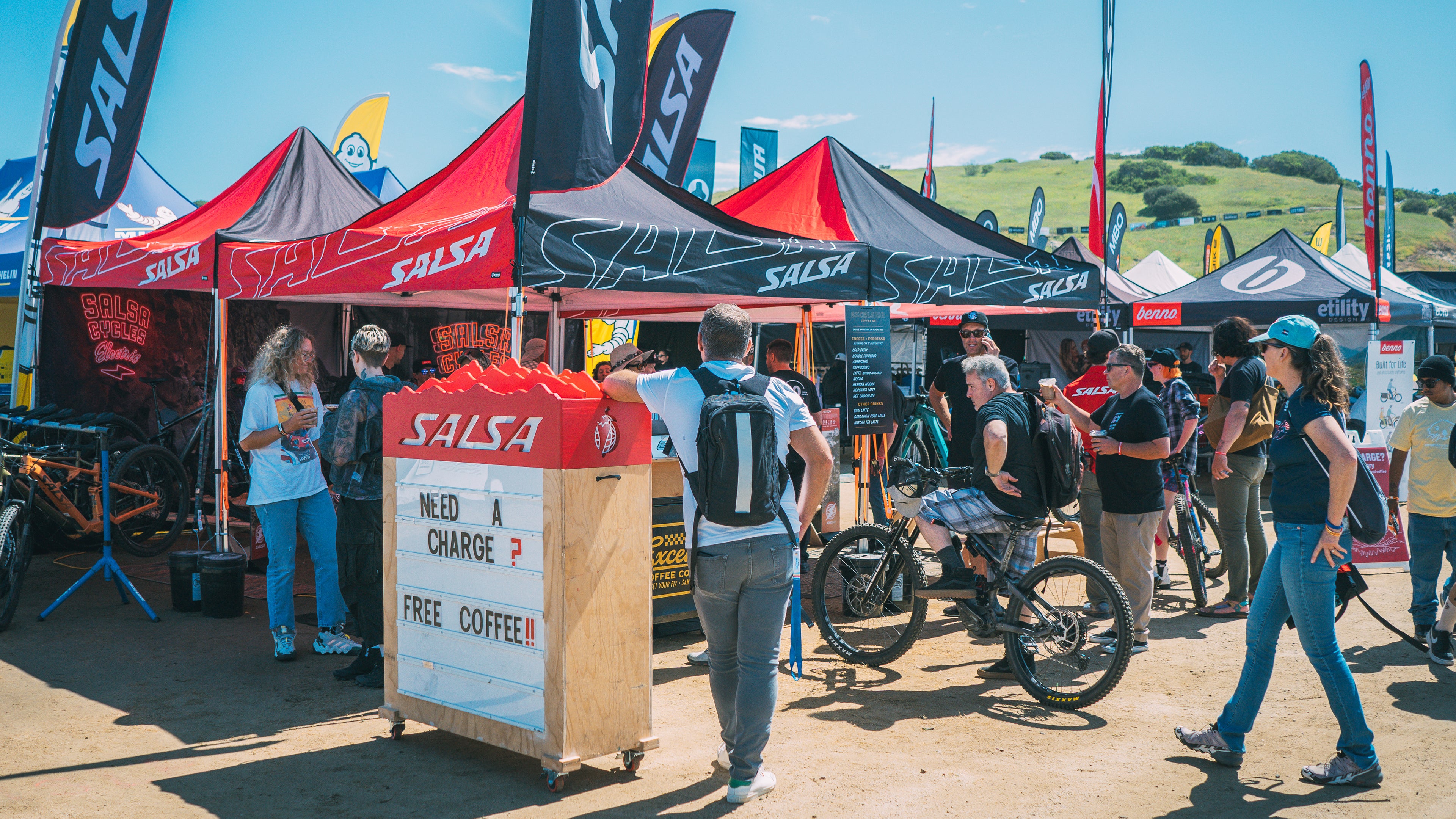 Salsa tents are set up at a cycling event. Many visitors approach the tents.