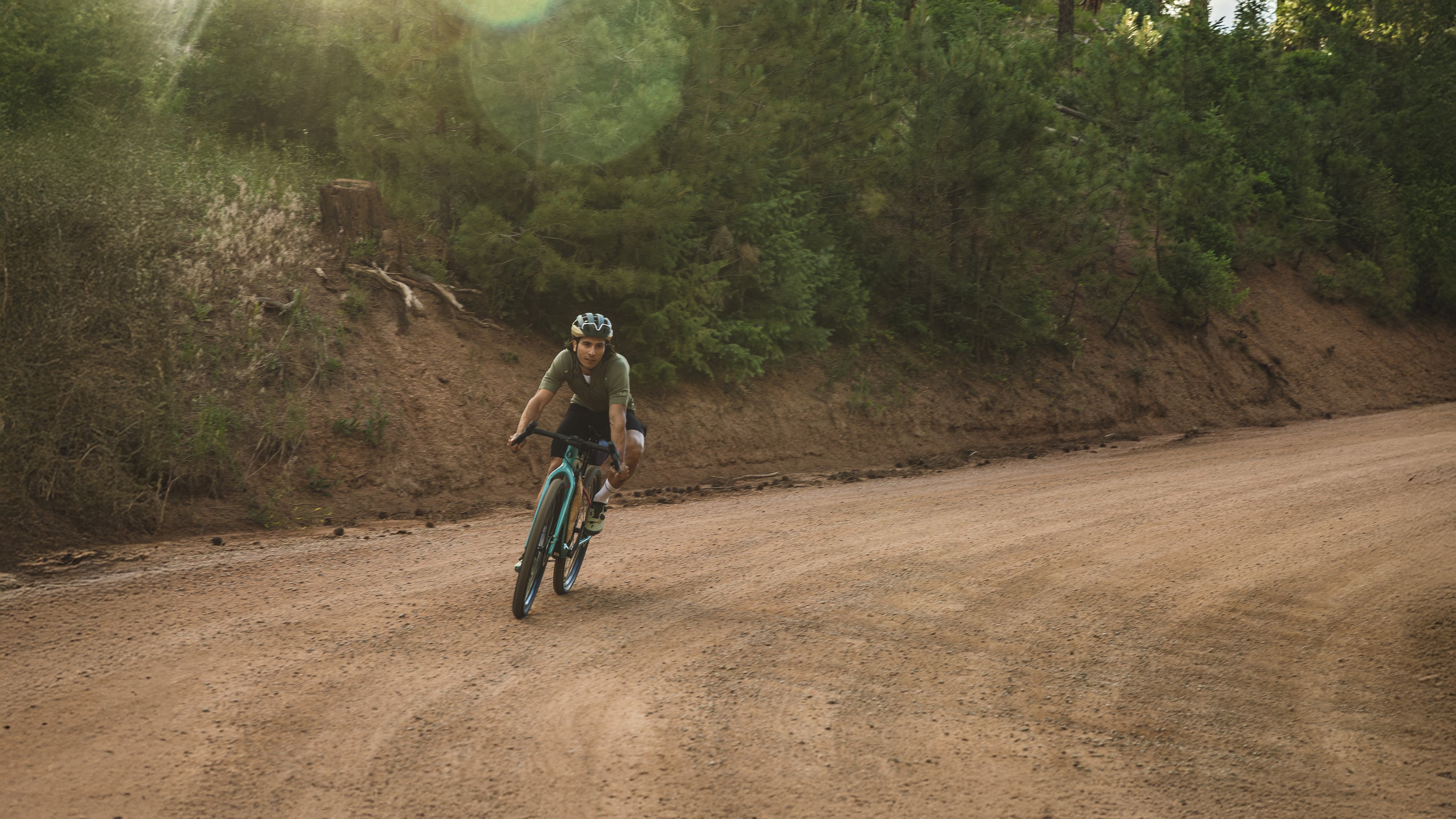 Cyclists on a turquoise Salsa drop bar bike rides around a curve on a gravel road.